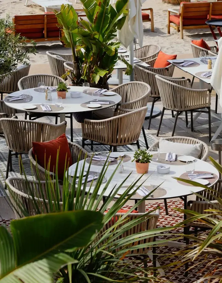 Round tables set for lunch with rope chairs and terracotta cushions on a beach terrace